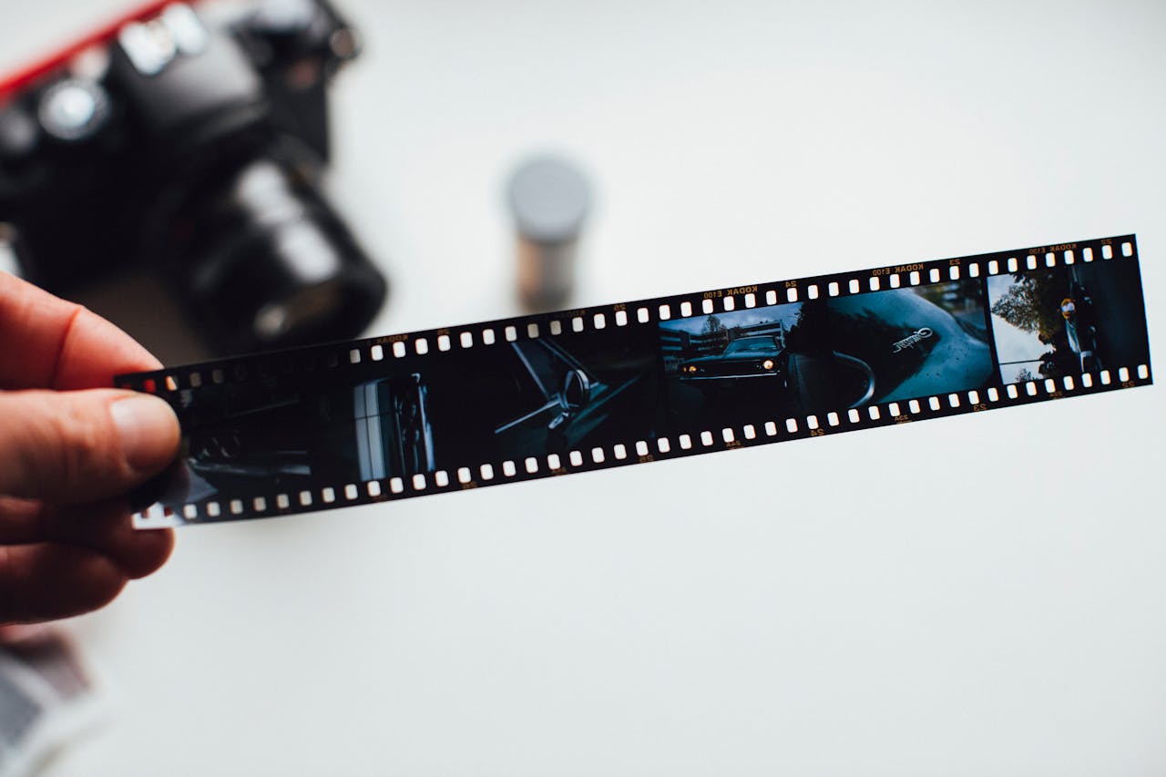 Close-up of a hand holding a vintage film strip with a blurred camera in the background, evoking nostalgia.