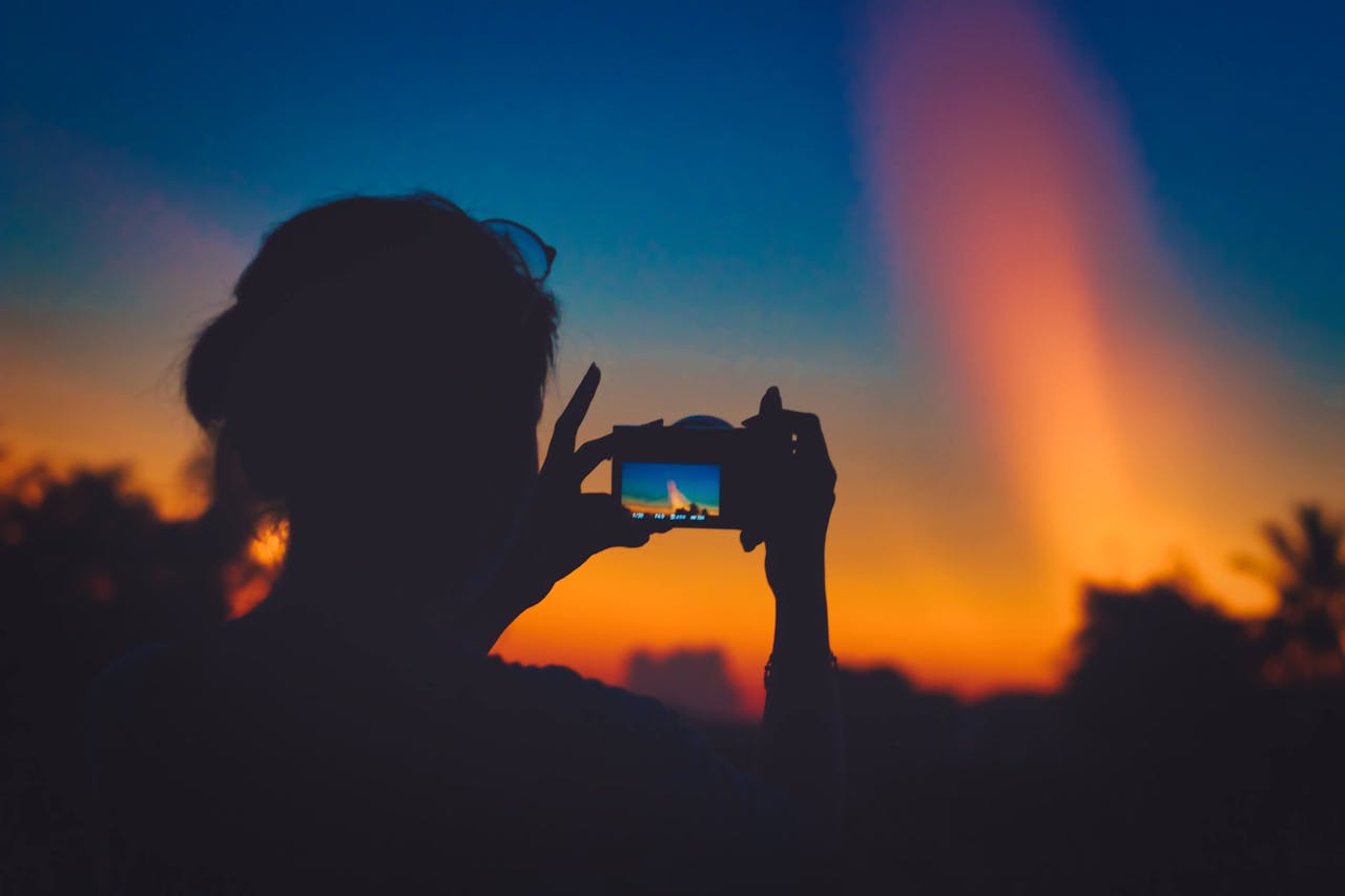 A woman captures a dramatic sunset with her smartphone, featuring vivid colors and a dramatic sky.